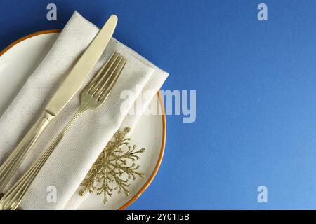 Beautiful Christmas setting with plate, elegant cutlery and golden snowflake on blue table, top view. Space for text Stock Photo