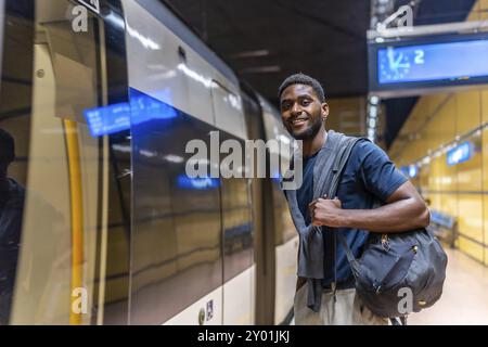 African young businessman waiting for the metro at night standing on the platform and smiling at camera Stock Photo