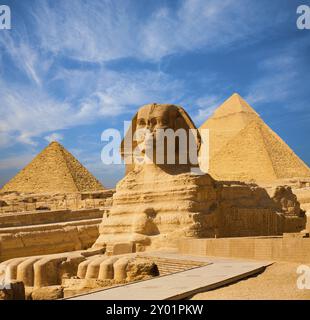 Egyptian Great Sphinx full body portrait with head, feet with all pyramids of Menkaure, Khafre, Khufu in background on a clear, blue sky day in Giza, Stock Photo