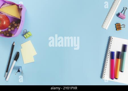 Primary school flat lay concept with assorted school supplies, notepad, pen, pencil, markets, stickers, paper clips and lunch box with sandwich, nuts Stock Photo