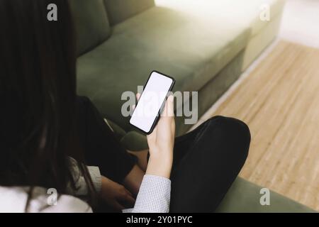 Communication concept with black hear girl sitting on green sofa and holding smartphone in her hand with empty white screen, sun beam on the front Stock Photo