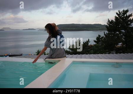 Dolsan-eup, Yeosu-si, South Korea - July 26, 2024: Young woman watching sunrise at a resort with a swimming pool overlooking the sea in Yeosu Stock Photo