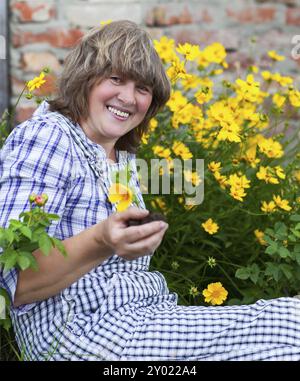 Happy middle aged woman with flowers working in her backyard garden Stock Photo