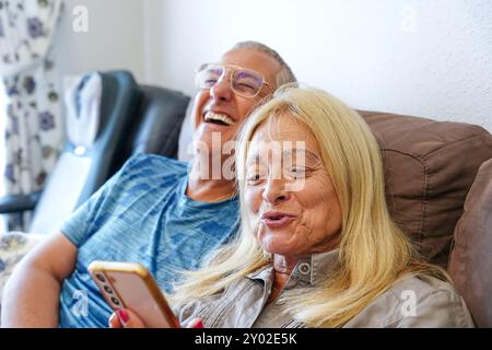 Happy mature couple laughing on sofa with mobile. Happy family Stock Photo