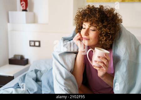 Relaxed lady holding cup of hot drink on bed Stock Photo