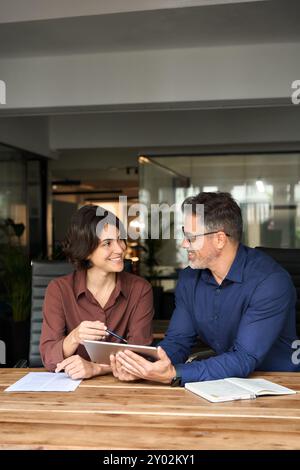 Two happy business colleagues having conversation at office meeting using tab. Stock Photo