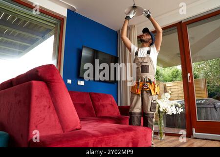 Male electrician finished mounting ceiling lamp - installing a fluorescent light bulb Stock Photo