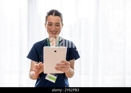 Happy female young doctor, cardiologist, using digital tablet and standing against white background Stock Photo
