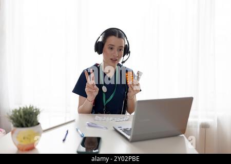Young beautiful female doctor wearing headphones, making online webcam video call on laptop screenand gives advice to patient. Videocall view. Tele me Stock Photo