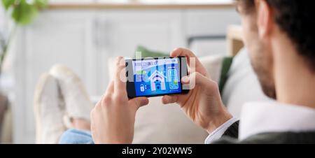 Young man holding mobile phone with smart home security system on screen Stock Photo