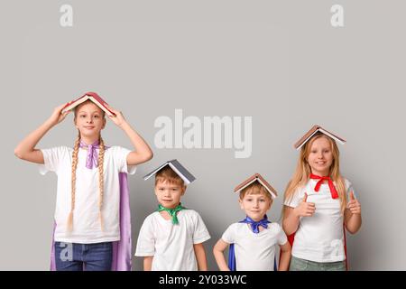 Cute kids dressed as superhero with books on grey background. Library Lovers Day Stock Photo