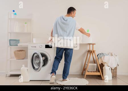 Young man taking bottle of detergent from table in laundry room Stock Photo