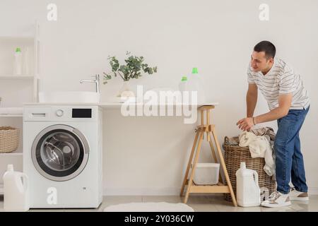 Young man taking dirty clothes from basket in laundry room Stock Photo