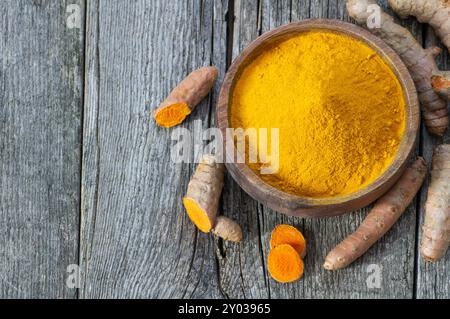 Turmeric powder in spoon or bowl and fresh turmeric root on wooden background, spice concept, ( curcuma longa ) Stock Photo