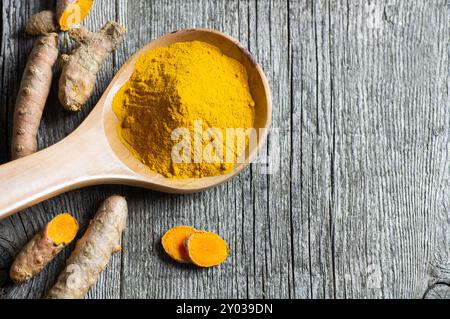 Turmeric powder in spoon or bowl and fresh turmeric root on wooden background, spice concept, ( curcuma longa ) Stock Photo