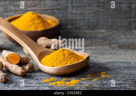 Turmeric powder in spoon or bowl and fresh turmeric root on wooden background, spice concept, ( curcuma longa ) Stock Photo