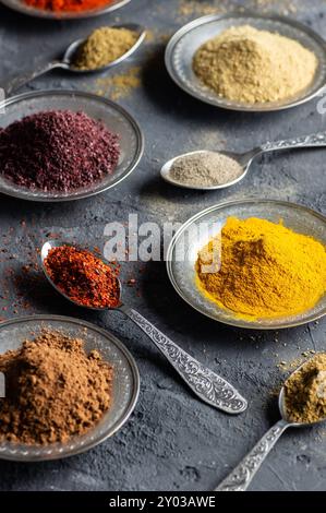 Assortment of natural spices on a vintage silver spoons or dishes on dark rustic stone background, Healthy spice concept Stock Photo