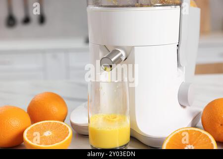 Modern juicer, oranges and glass on white table in kitchen, closeup Stock Photo