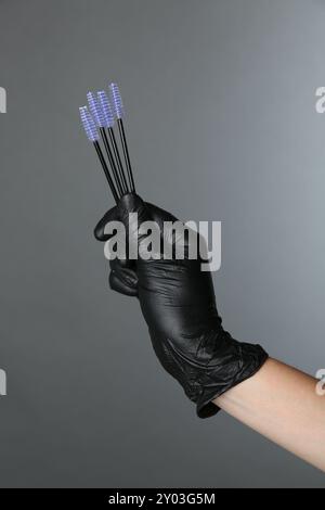 Professional cosmetologist holding disposable makeup brushes on grey background, closeup Stock Photo