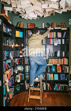 Rear view of young man choosing books while standing on ladder in bookstore Stock Photo