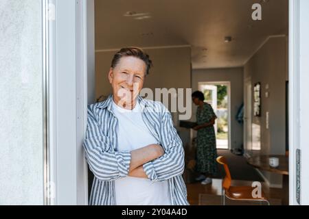 Portrait of smiling senior man leaning with arms crossed on doorway Stock Photo