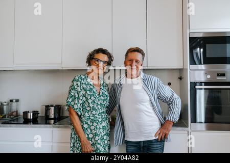 Portrait of smiling elderly couple standing in kitchen at home Stock Photo
