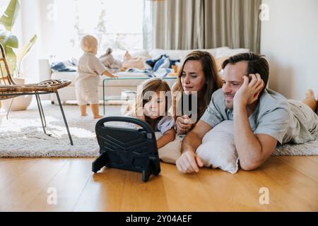 Father and mother watching tablet PC while lying down with daughter on floor at home Stock Photo