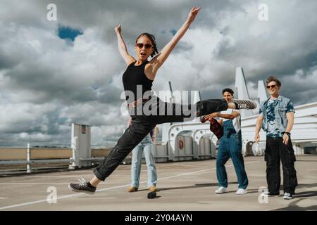 Portrait of young woman in casuals doing split in parking lot under cloudy sky Stock Photo