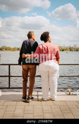 Rear view of female nurse standing with senior man near railing on pier against sky Stock Photo