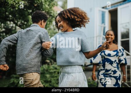Carefree sister dancing arm in arm with brother during garden party Stock Photo