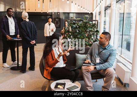 Multiracial male and female delegates discussing business strategies while sitting on sofa at convention center Stock Photo