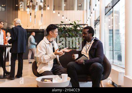 Young male entrepreneur discussing with businessman sitting on sofa during seminar at convention center Stock Photo