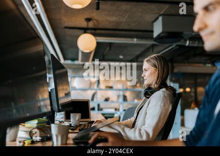 Young female programmer doing coding while sitting at desk in office Stock Photo