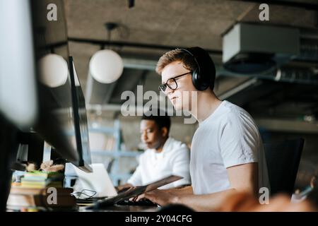 Young male programmer doing coding on computer with wireless headphones in office Stock Photo