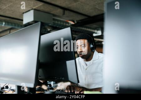 Focused young businessman with wireless headphones doing coding on computer at office Stock Photo