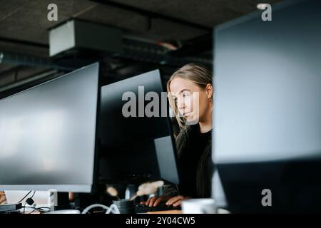 Focused female programmer doing coding on computer while sitting at desk in office Stock Photo