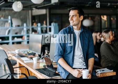 Smiling young businessman looking away with coffee cup in tech startup office Stock Photo