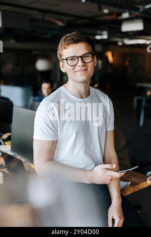 Portrait of smiling young tech entrepreneur with smart phone in workplace Stock Photo