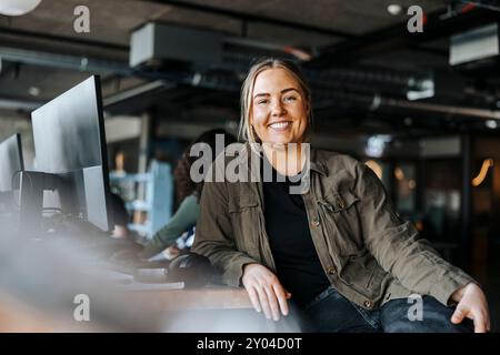 Portrait of happy female tech programmer leaning on desk sitting at office Stock Photo