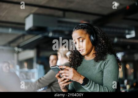 Young female tech programmer wearing headphones using smart phone at office Stock Photo