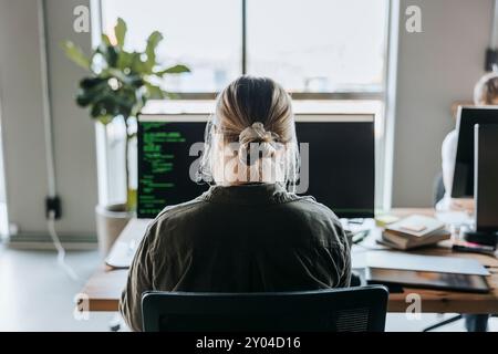 Rear view of female programmer coding on computer while sitting at desk in office Stock Photo