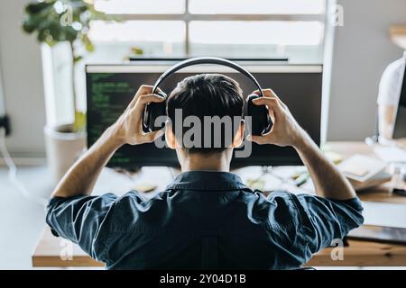 Rear view of male programmer wearing headphones in office Stock Photo
