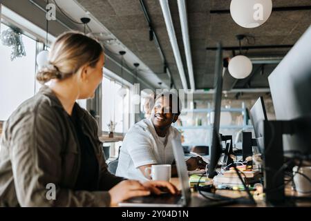 Female programmer talking with male colleague while working in tech startup office Stock Photo