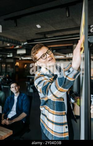 Businessman sticking adhesive notes on whiteboard while conducting meeting in office Stock Photo