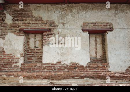 A close-up view of an aged brick wall with patches of plaster peeling off, revealing the underlying structure. Stock Photo