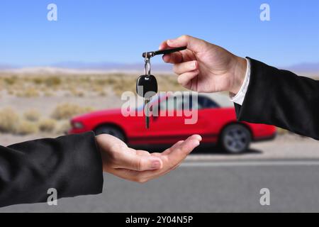 A hand giving a key to another hand. Both persons in suits. Car in the background Stock Photo