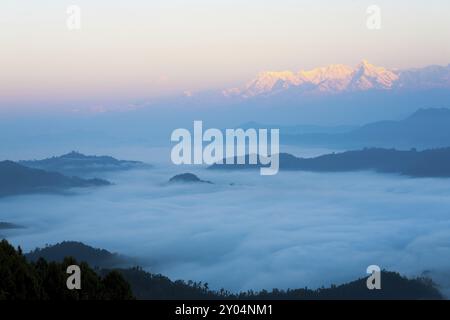 Tops of distant Himalayan mountain peaks glow red from morning sunrise light above an undulating sea of clouds seen from Bandipur, Nepal, Asia Stock Photo