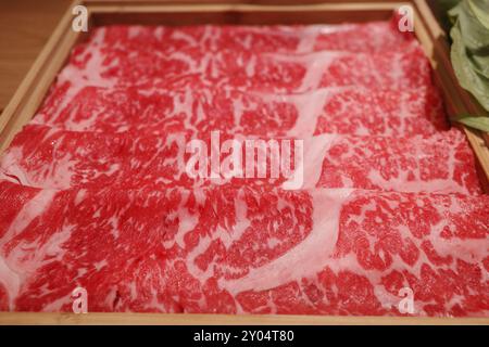 A close-up image showcasing thinly sliced marbled Wagyu beef arranged neatly in a wooden tray. Stock Photo