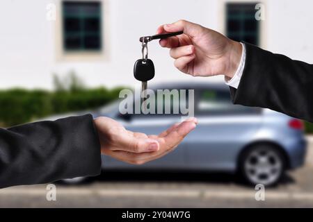 A hand giving a key to another hand. Both persons in suits. Car in the background Stock Photo