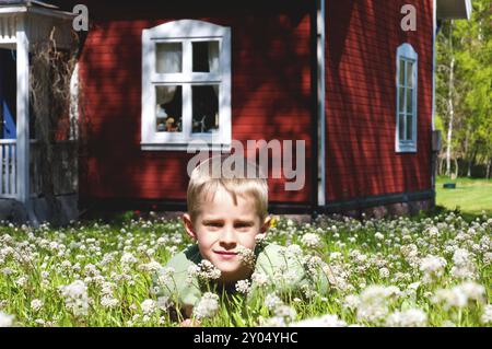 Small boy lying on a meadow in spring in front of an old red .wooden house in Sweden Stock Photo